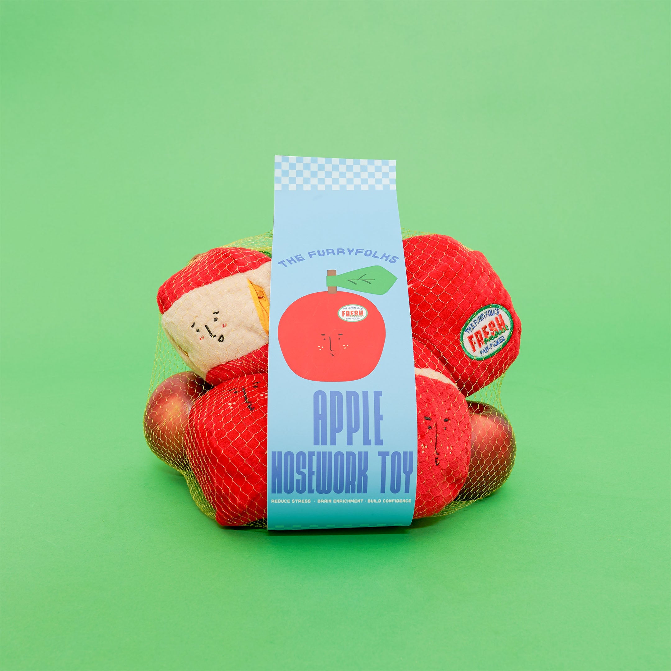  A mesh bag of red apple-shaped dog toys with a label reading "The Furryfolks Apple Nosework Toy" against a green background.
