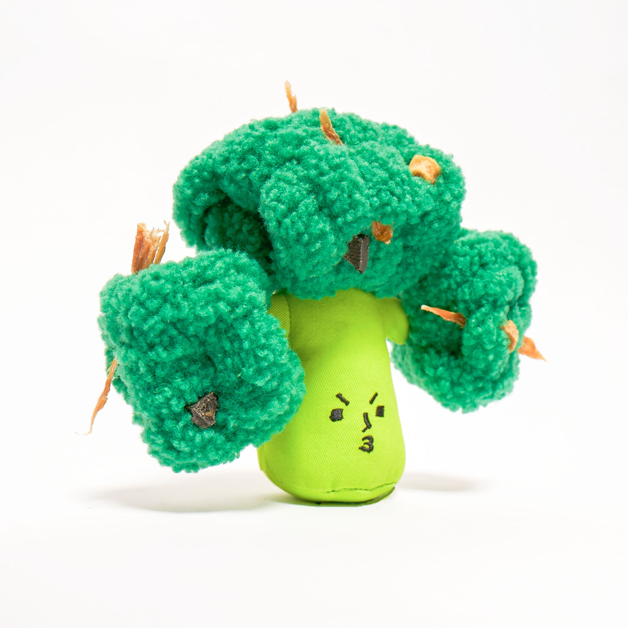 The image displays a dog nosework toy designed to look like a piece of broccoli, with a cheerful face on the green top. The toy’s green sections likely have pockets or compartments where treats can be hidden to encourage a dog’s natural foraging instincts. The texture of the toy is visually similar to broccoli florets, adding to its playful appearance. The white background highlights the toy's vibrant color and intricate details, making it an attractive accessory for pet enrichment activities.