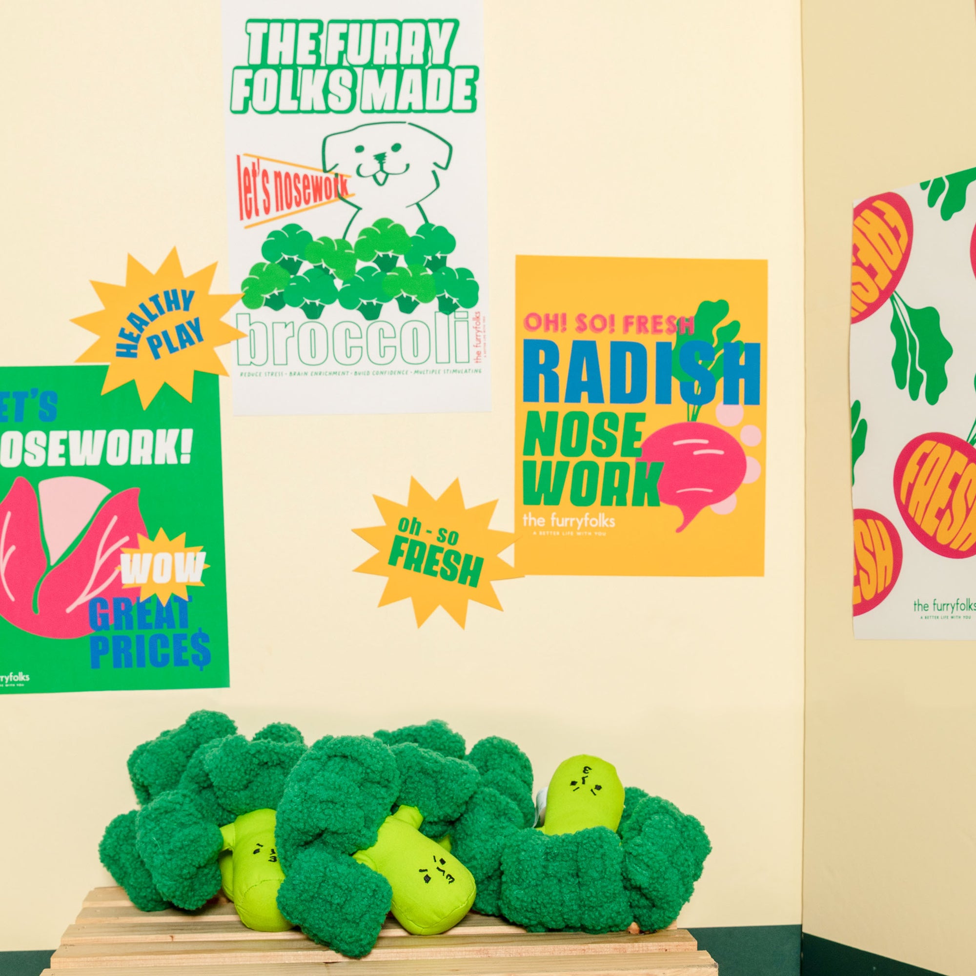 A display of broccoli dog toys with colorful promotional nosework posters in the background.