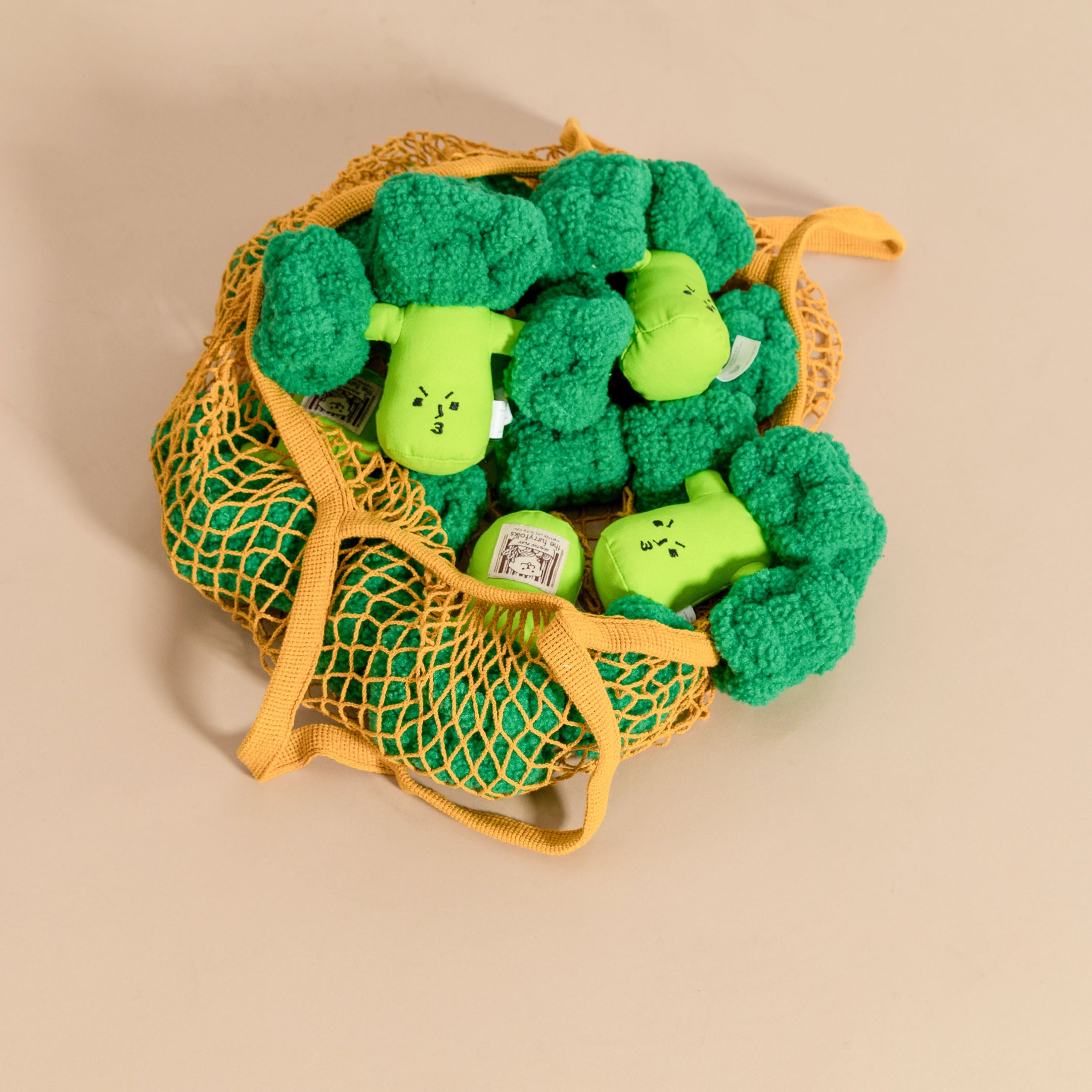 Yellow mesh bag filled with broccoli-shaped dog toys on a tan background.