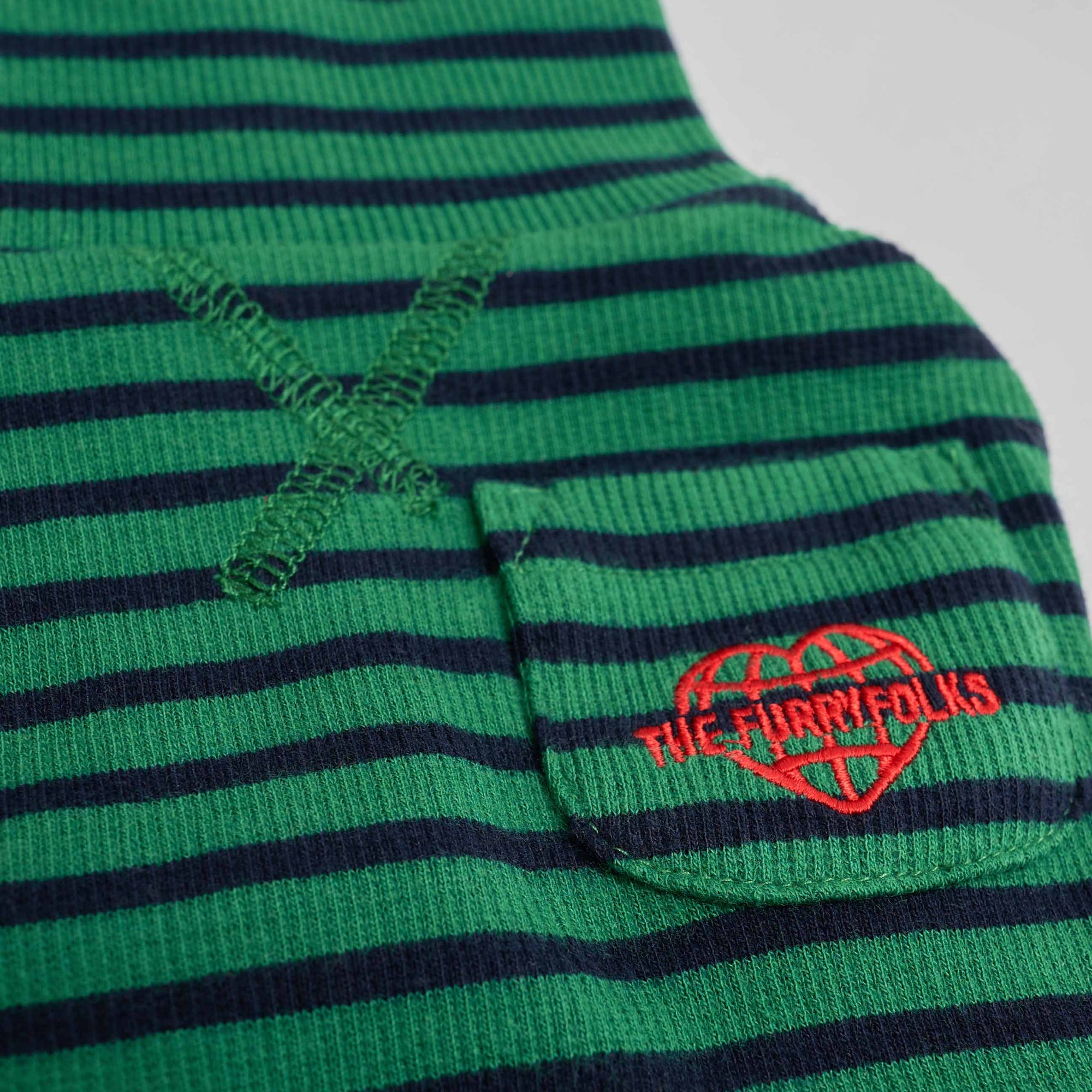Close-up of green and navy dog shirt fabric with 'THE FURRYFOLKS' logo embroidery and decorative cross-stitch detail.