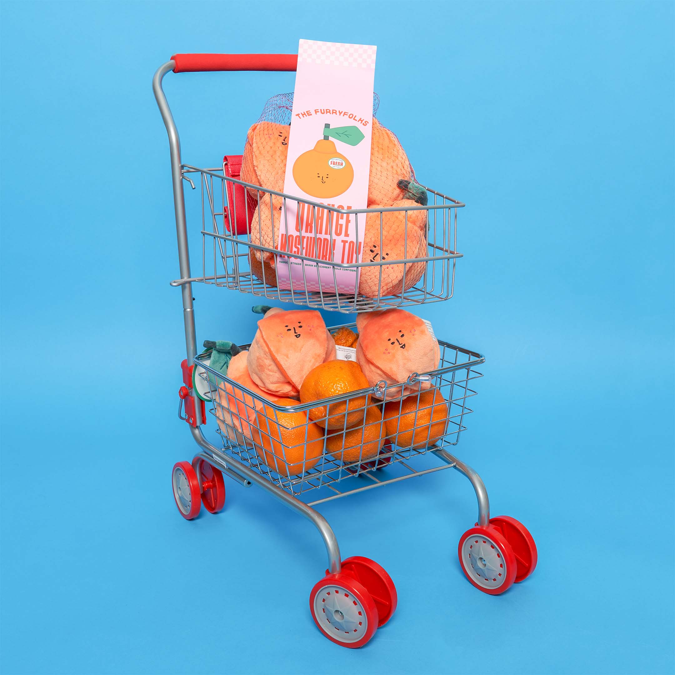 A miniature shopping cart filled with orange-shaped dog toys and oranges, with a label reading "The Furryfolks Orange Nosework Toy", set against a blue background.