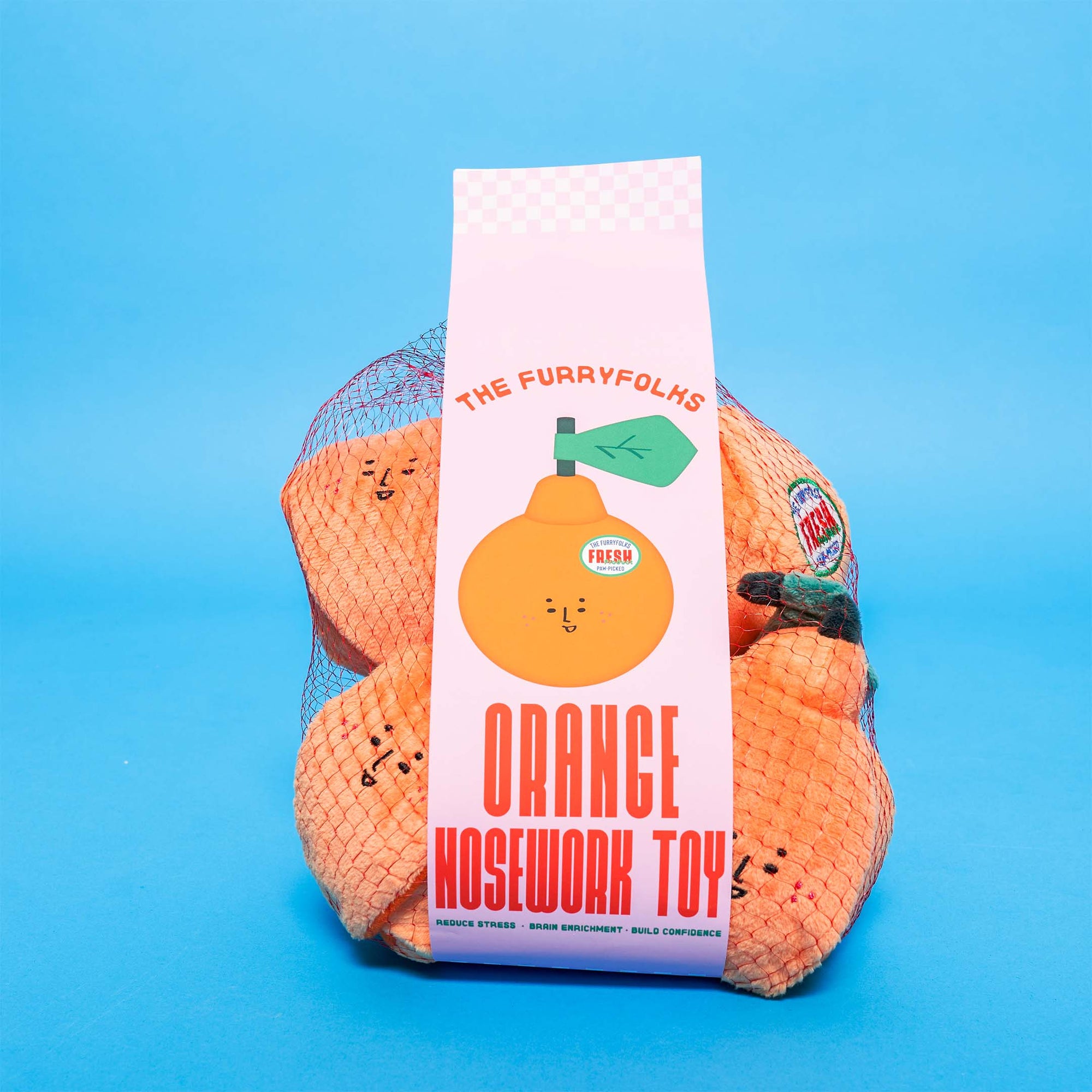 A mesh bag of orange-shaped dog toys on a blue background, with a label that reads "The Furryfolks Orange Nosework Toy," suggesting freshness and fun for pets.
