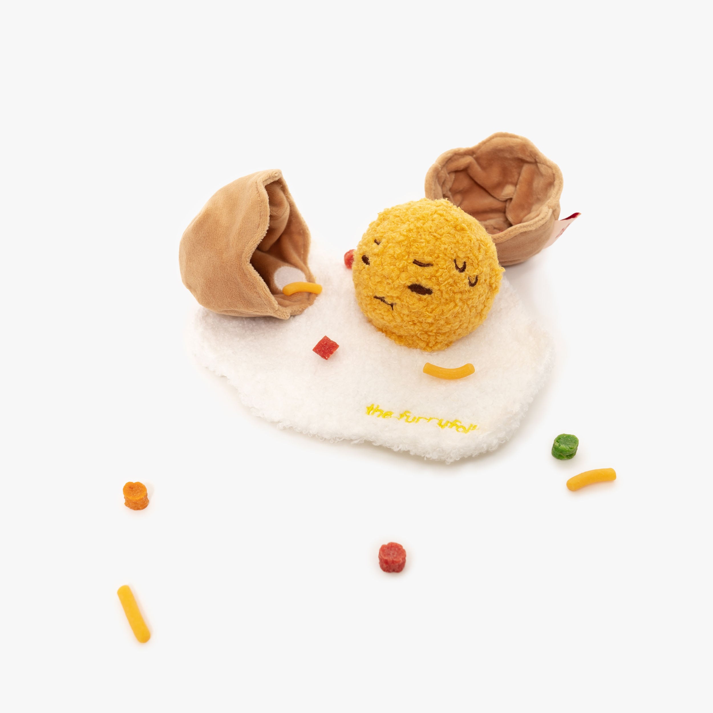 Engaging dog toy set featuring a charming plush egg with a smiling face, nestled on a white, fluffy base resembling an egg white. The toy is embroidered with 'The Furryfolks' branding, signaling quality and fun for pets.