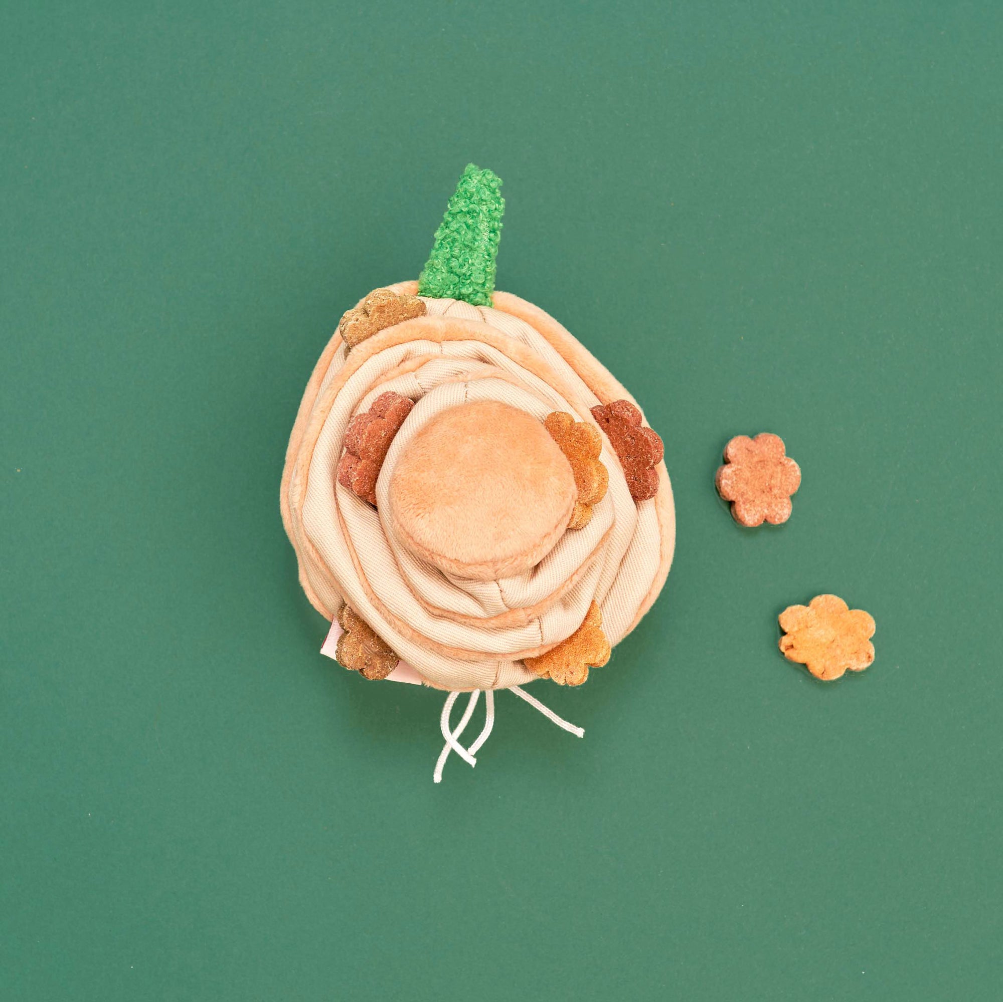 This is a neatly arranged image of a yellow onion-shaped dog toy with green leaves on top, against a green background. The toy is opened to reveal layers and compartments, with some dog treats placed around it, suggesting its use for interactive nosework or treat-finding games with pets. The color contrast and composition are visually appealing, emphasizing the toy's design and function.