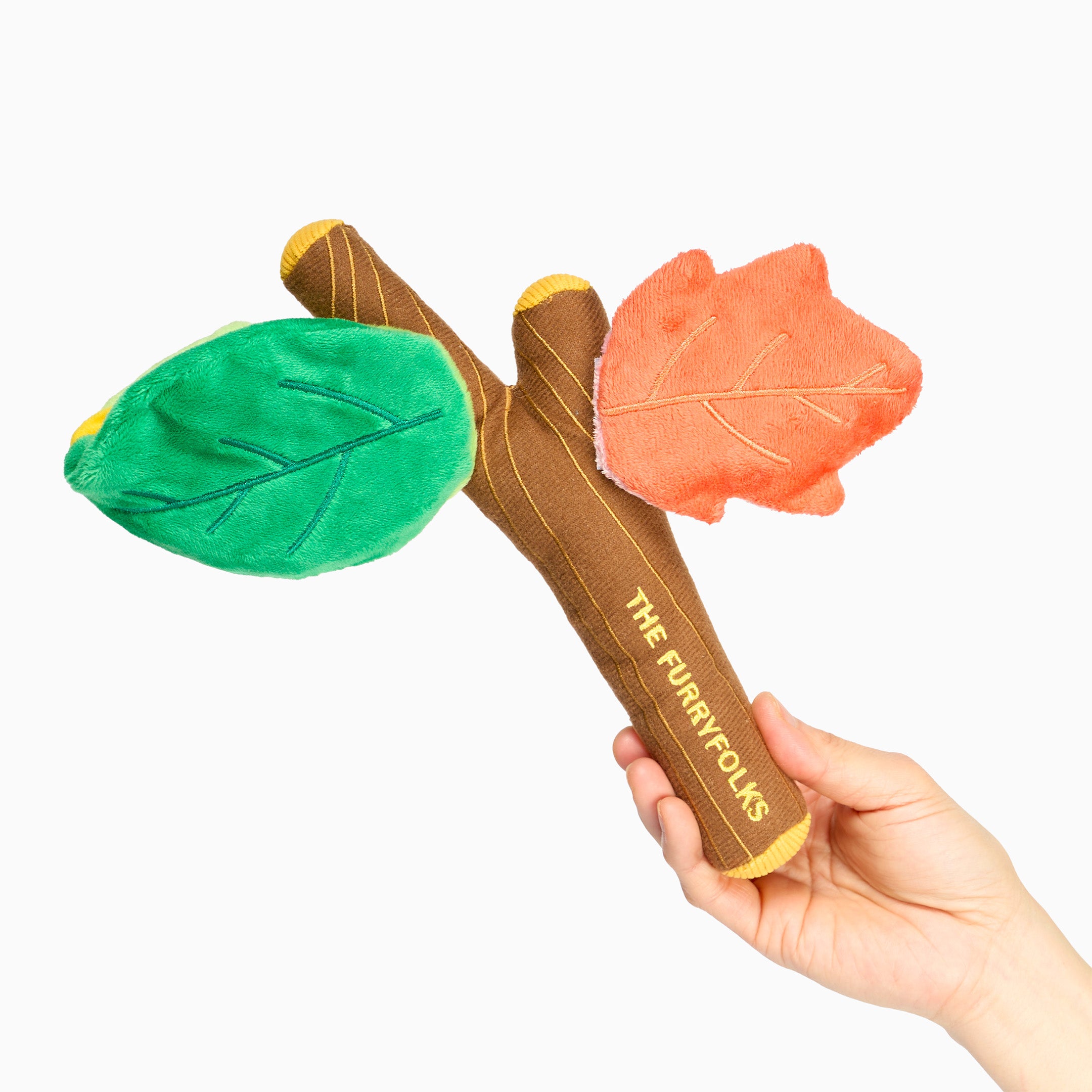 Hand holding a leaf-shaped toy with 'The Furry Folks' branding on a white background