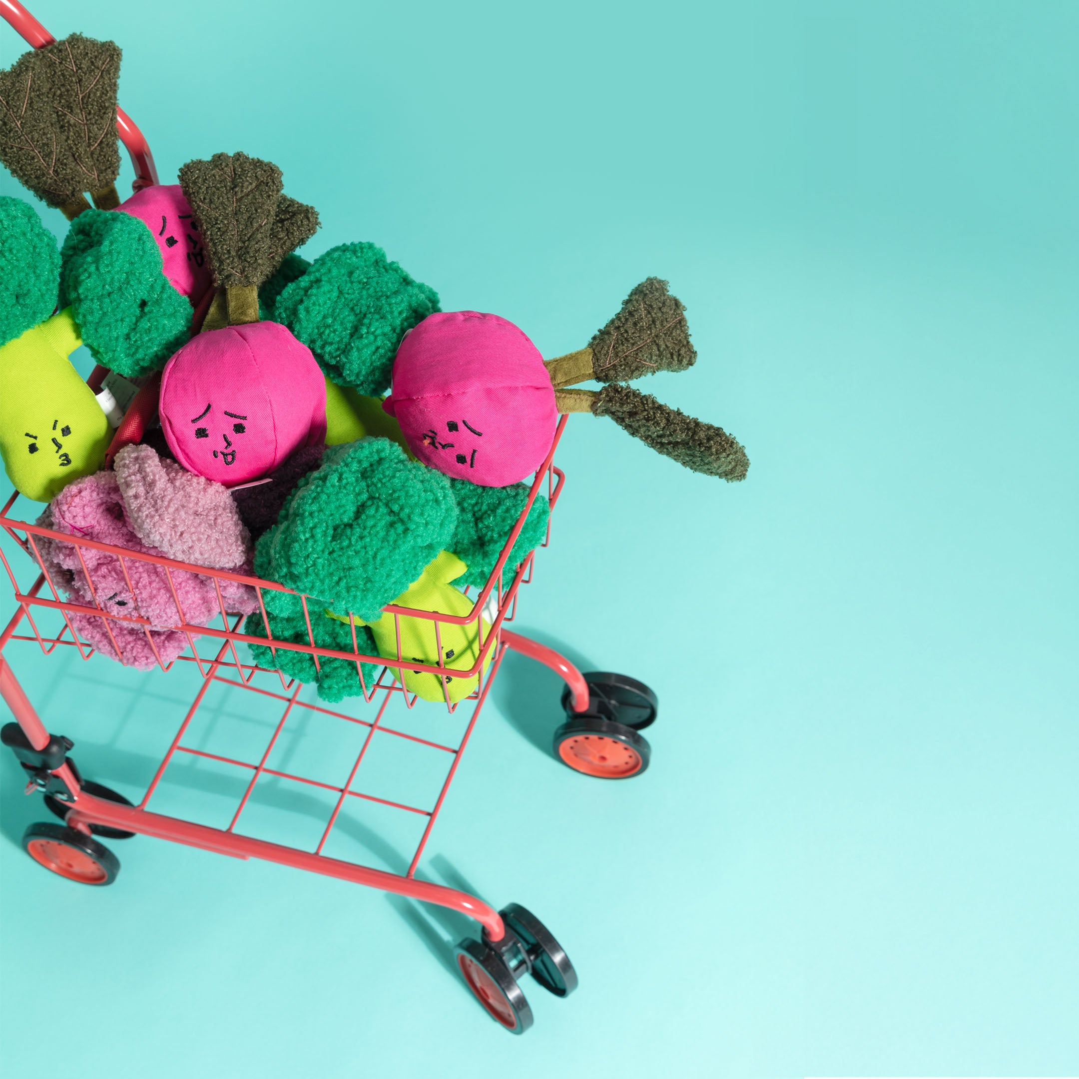 Colorful toy vegetables in a small shopping cart on a light blue background