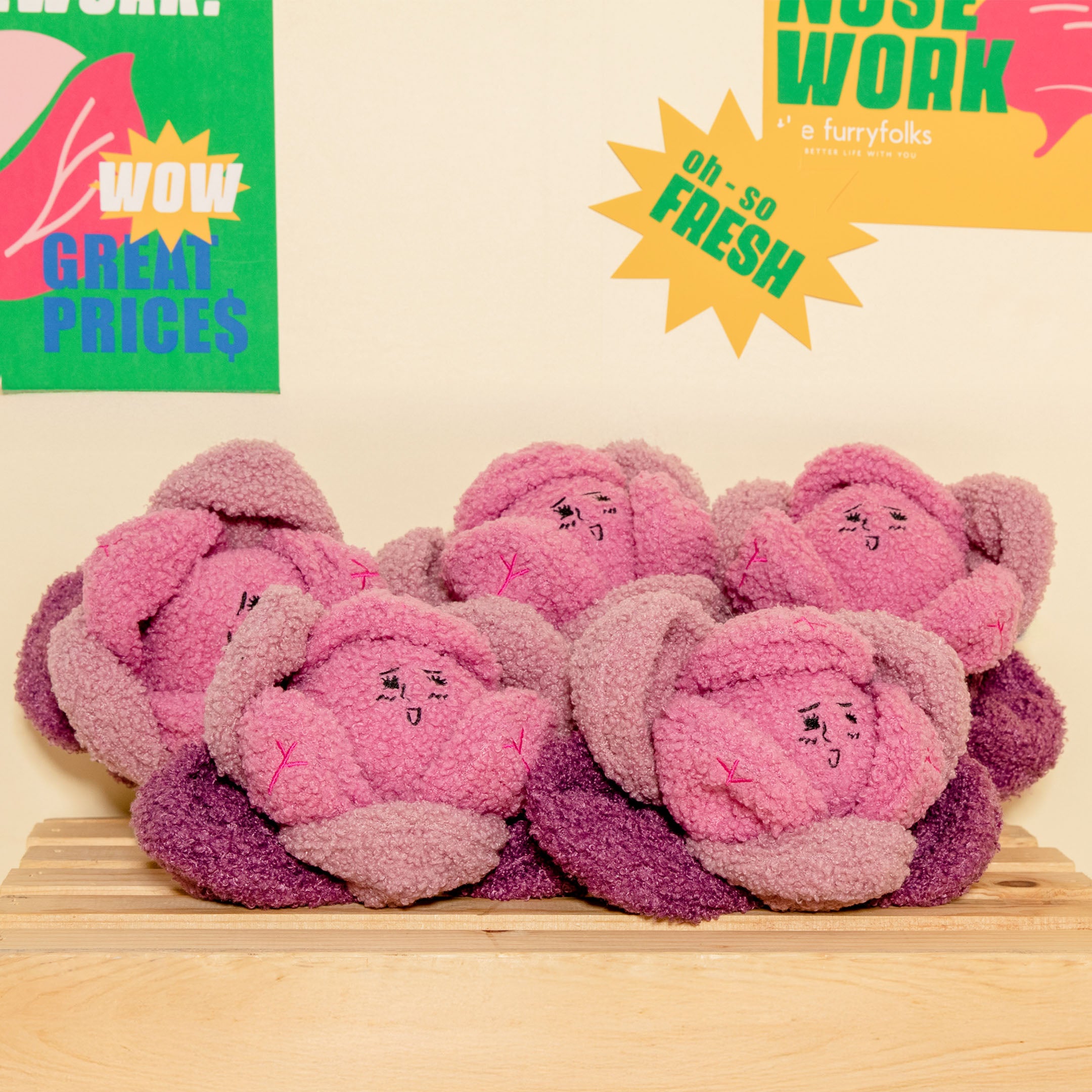 Pink plush toys resembling flowers on a wooden surface with promotional text in the background.