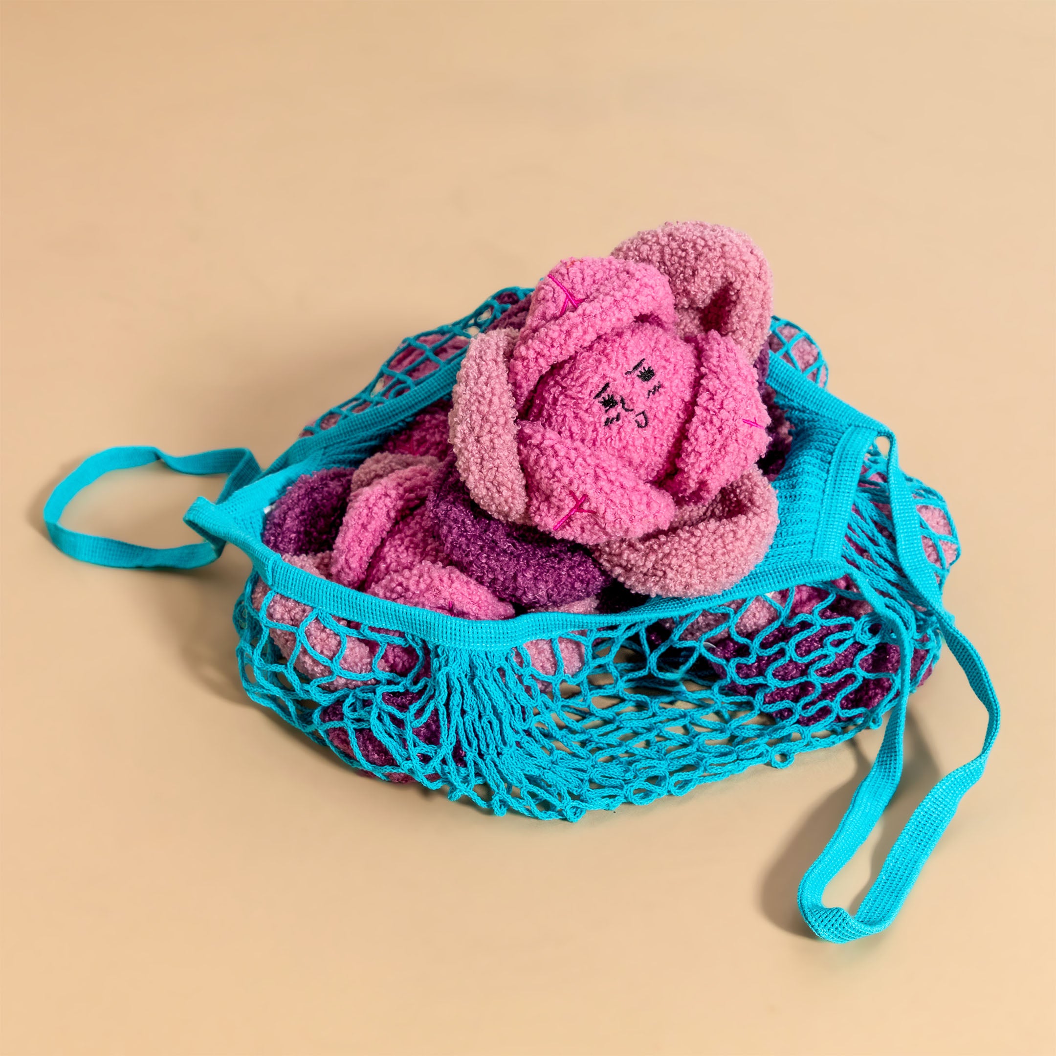 Pink plush toy in a blue mesh bag on a beige background