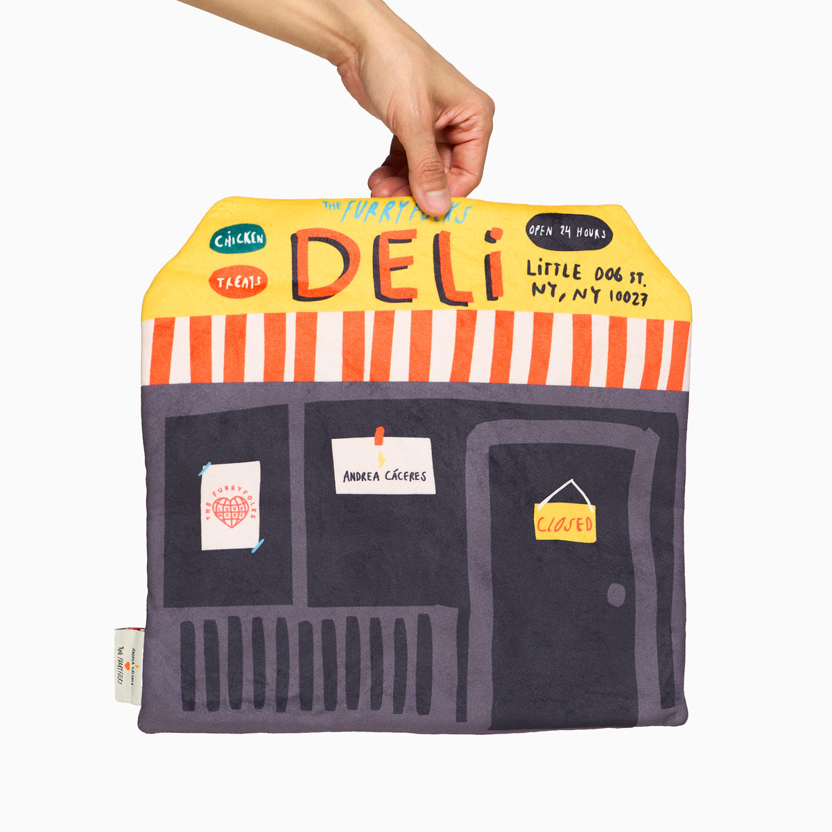 Back of the Deli Nosework mat held upright by one hand, featuring a yellow DELI sign, red-and-white striped awning, and purple door with a CLOSED sign.