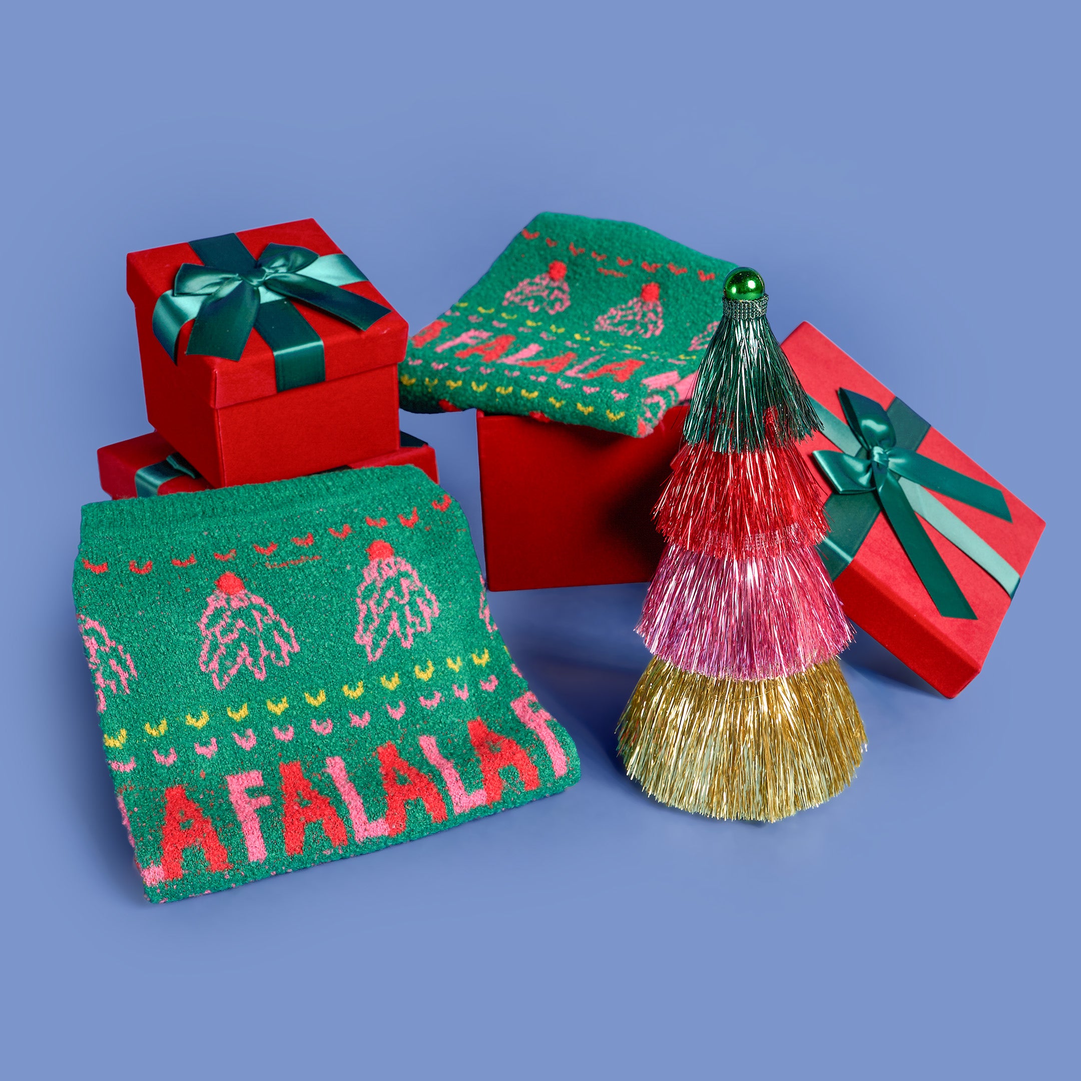 Decorative Christmas items including a red gift box, green pouch with 'A Falala' text, and a gold and pink ornament on a blue background.