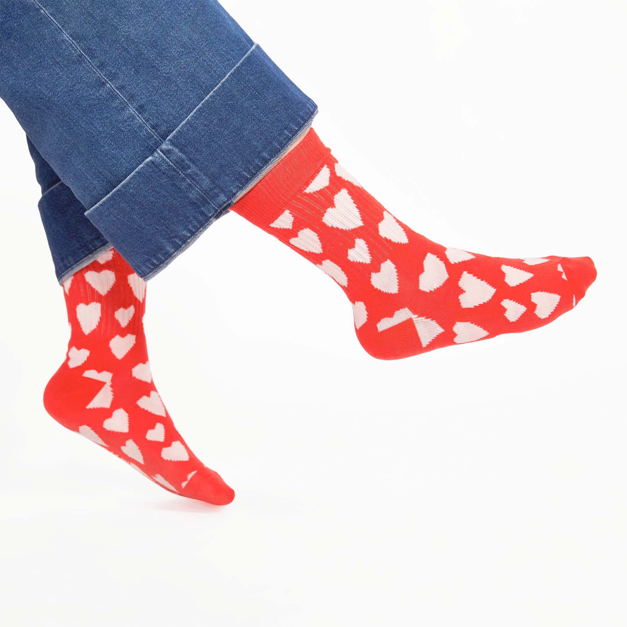 A close-up of vibrant red socks with playful abstract heart patterns, paired with cuffed denim jeans, showing off a fun and stylish look.