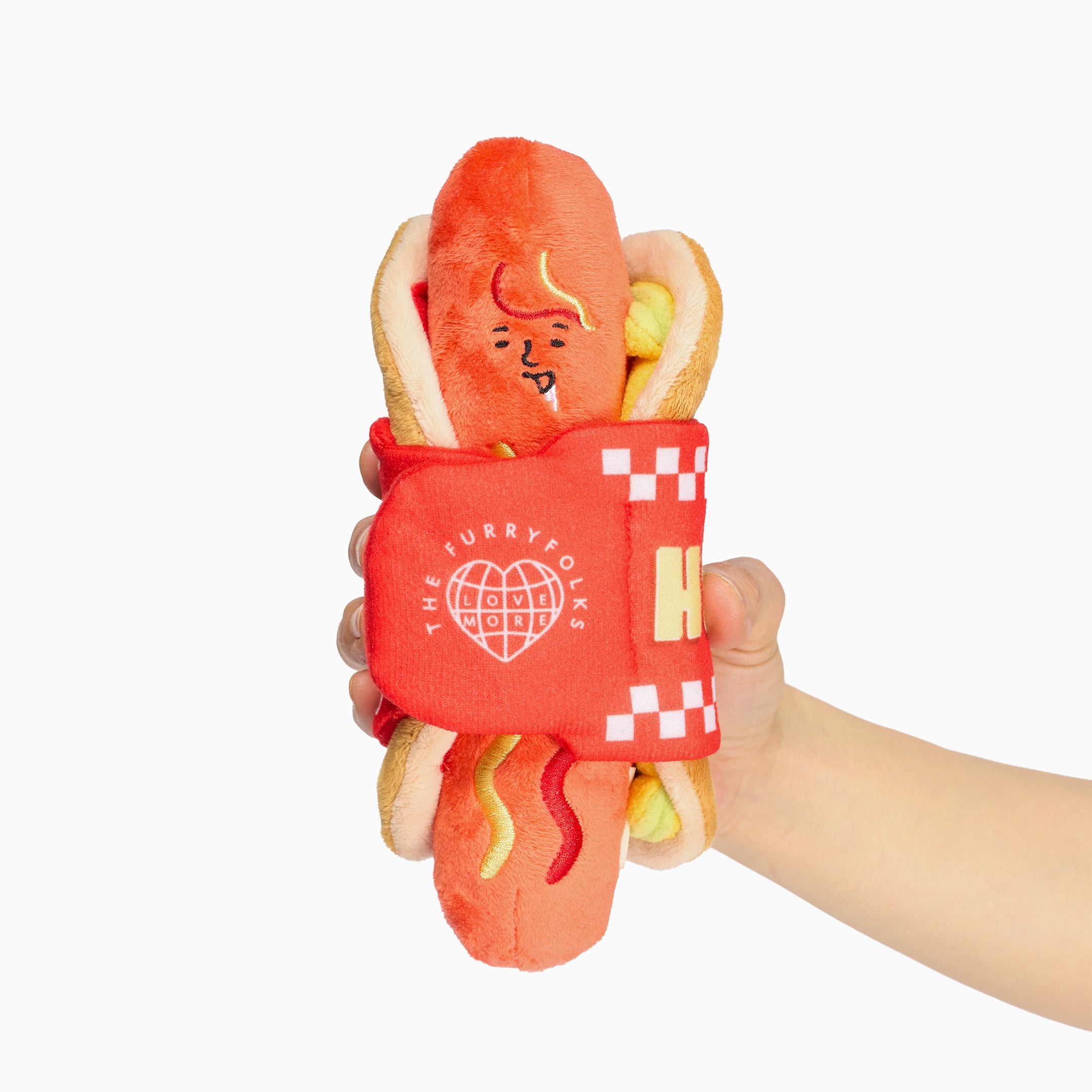 Plush toy resembling a hot dog with a bun, mustard, and ketchup held by a hand on a white background.