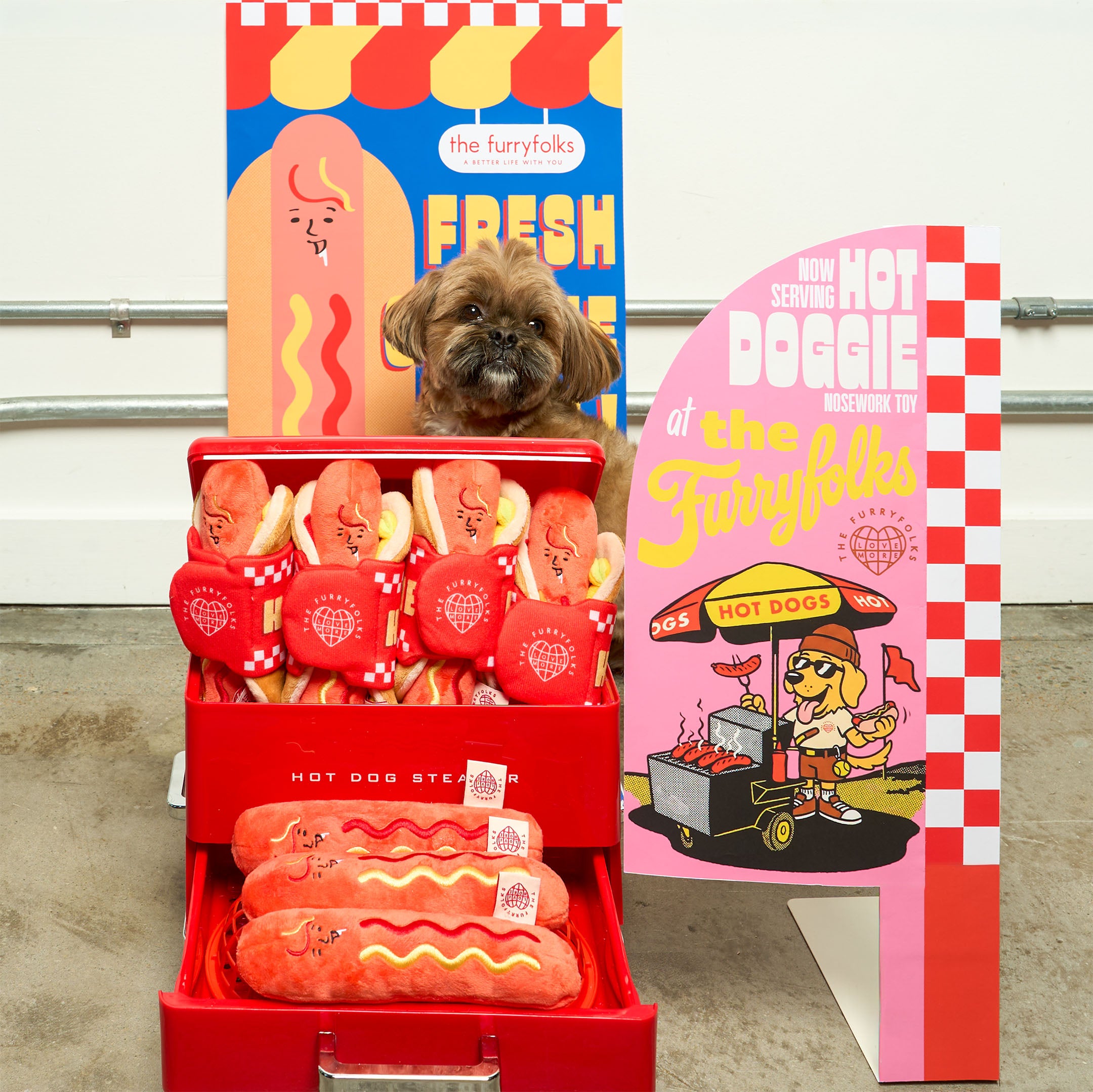 Dog sitting behind a red hot dog stand with cartoon hot dogs and a colorful backdrop featuring 'The Furry folks' branding.