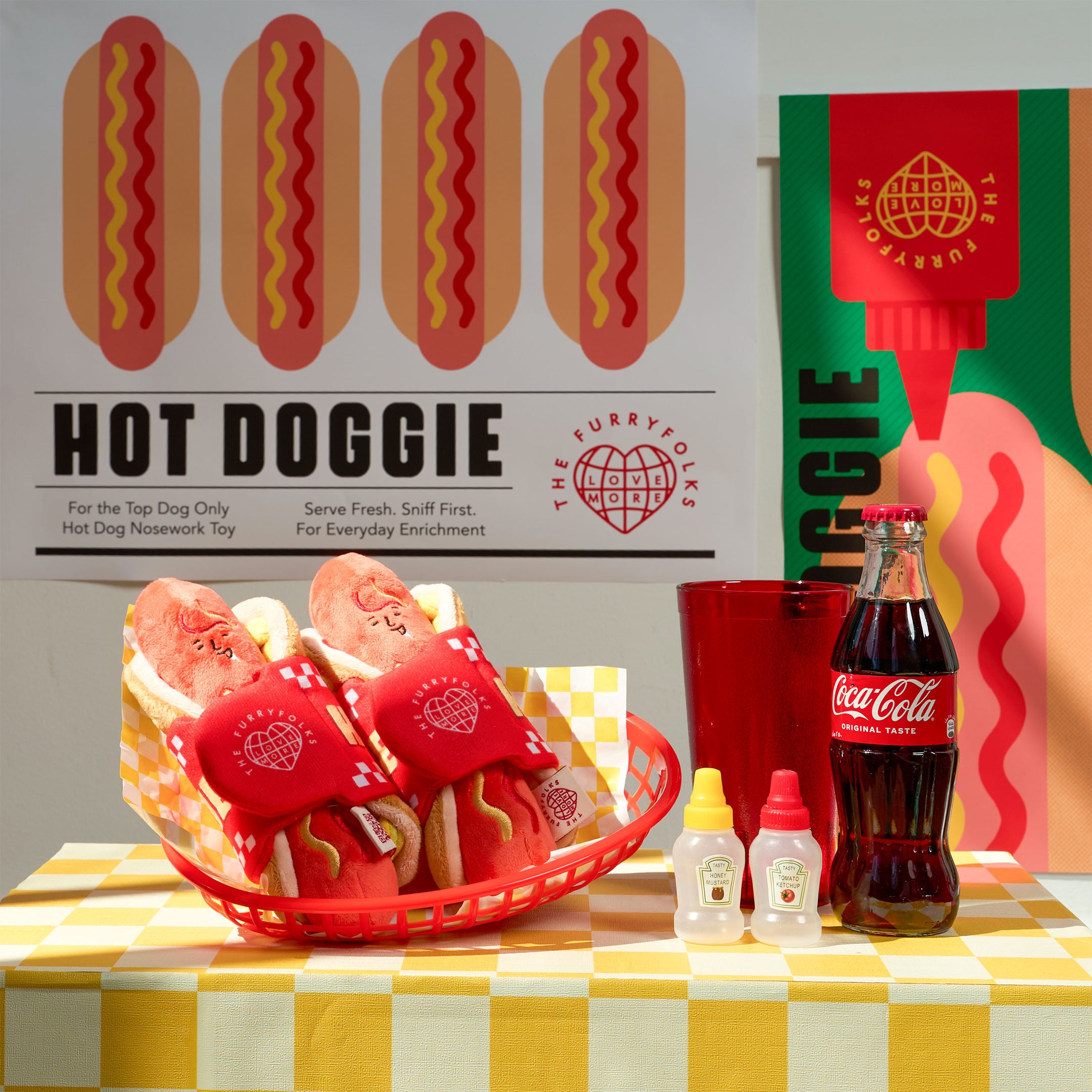 Hot dog toy set with Coca-Cola bottle on a checkered tablecloth, branded 'HOT DOGGIE'.