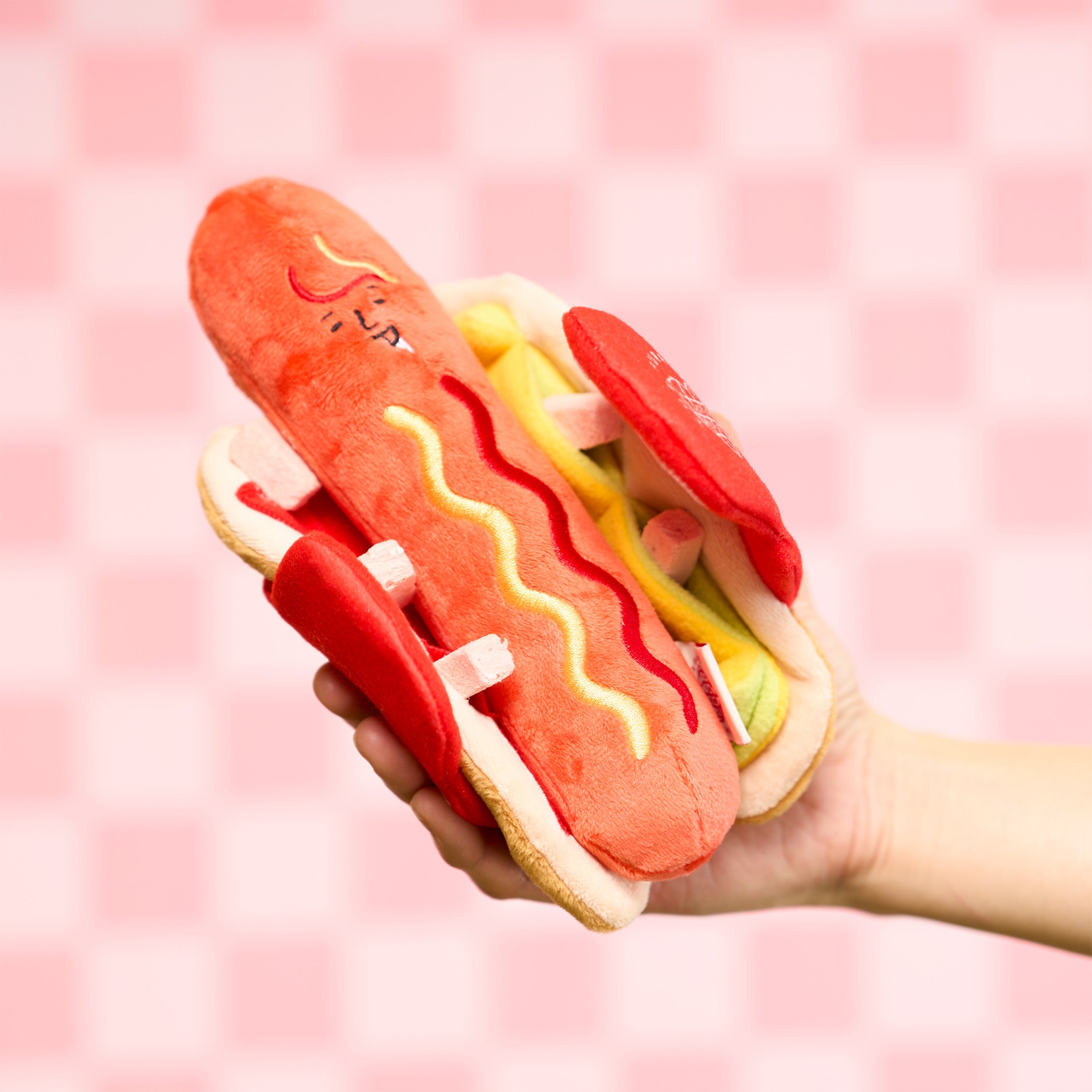 Plush toy shaped like a hot dog with a pink checkered background