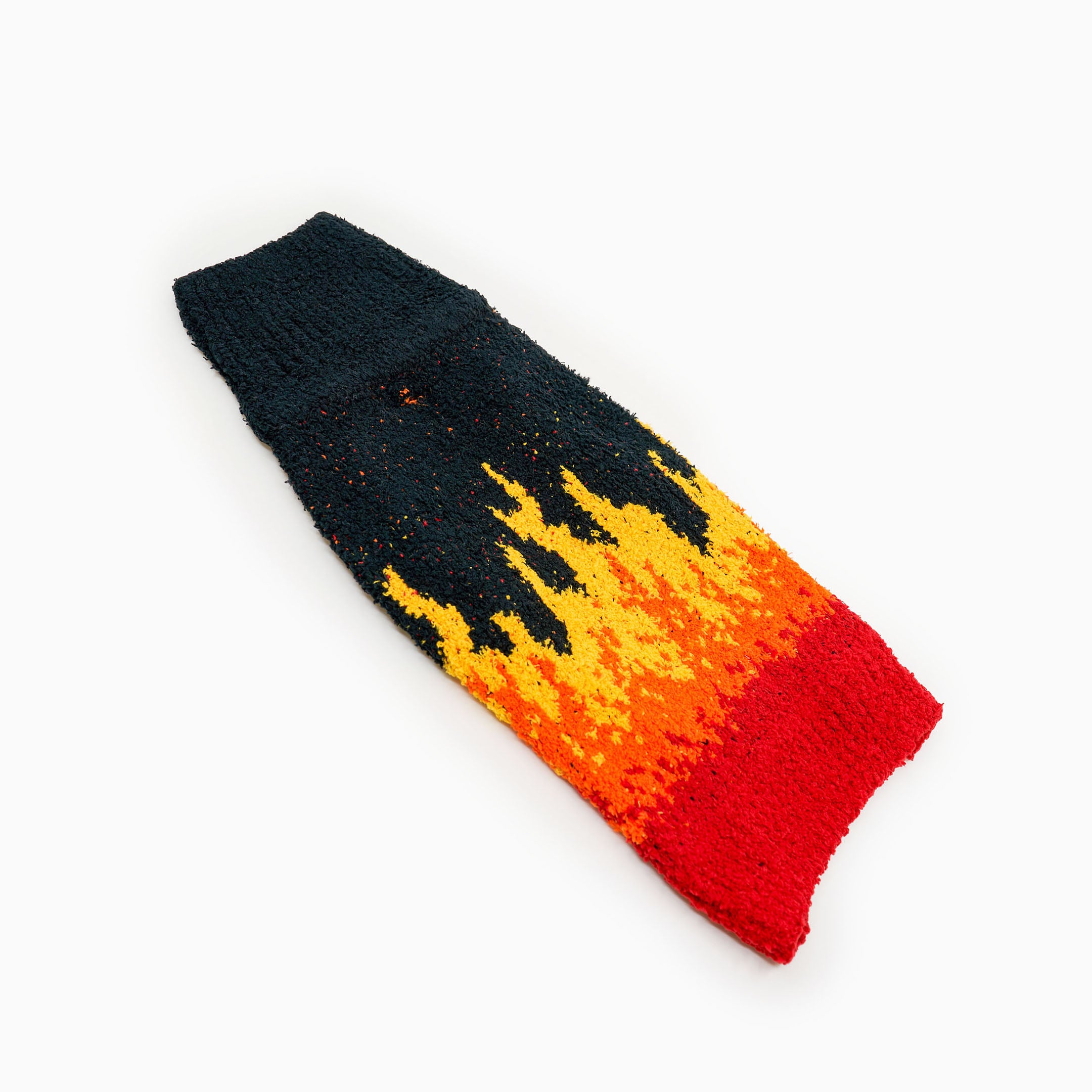 A vibrant, flame-patterned dog sweater is laid flat against a white background. The design features a striking gradient from deep black at the neck area, transitioning through yellow, orange, and finally to red at the bottom. The flame design creates a dynamic visual effect as it moves from the black into the fiery tones. The sweater appears soft and textured, likely made of a warm, cozy material.