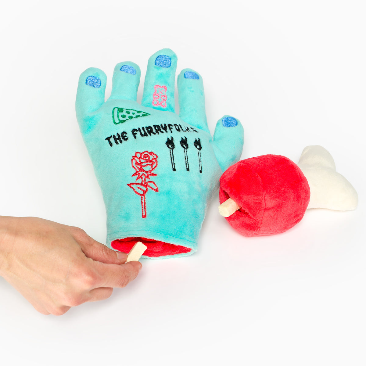 A person placing a treat inside the wrist of the Lost Hand dog toy, with the removable bone piece beside it.