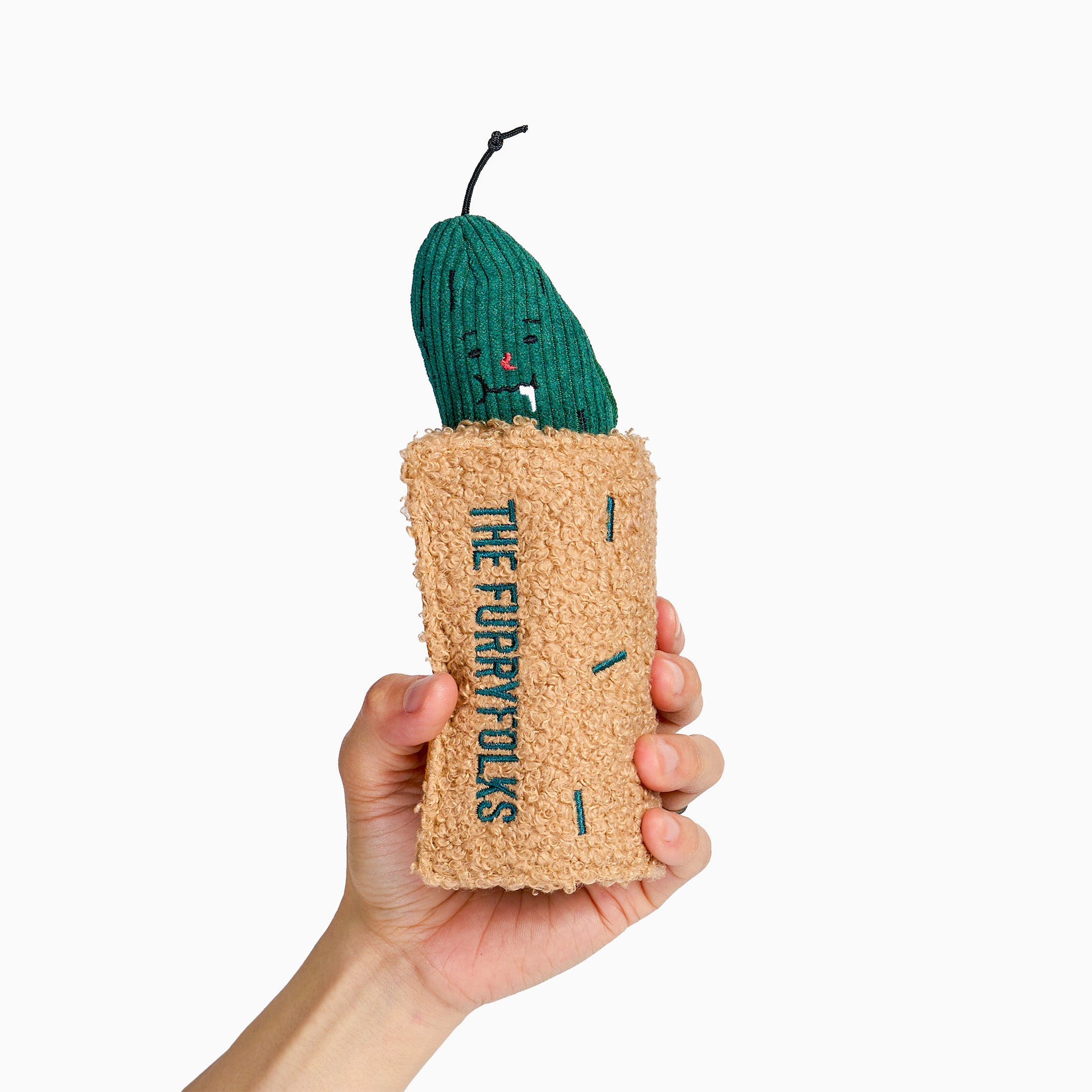 A hand holding a novelty phone case designed to look like a cactus. The case has a textured beige body with 'THE FURRYFOLKS' printed vertically in teal, and a green cactus top with small embroidered facial features.