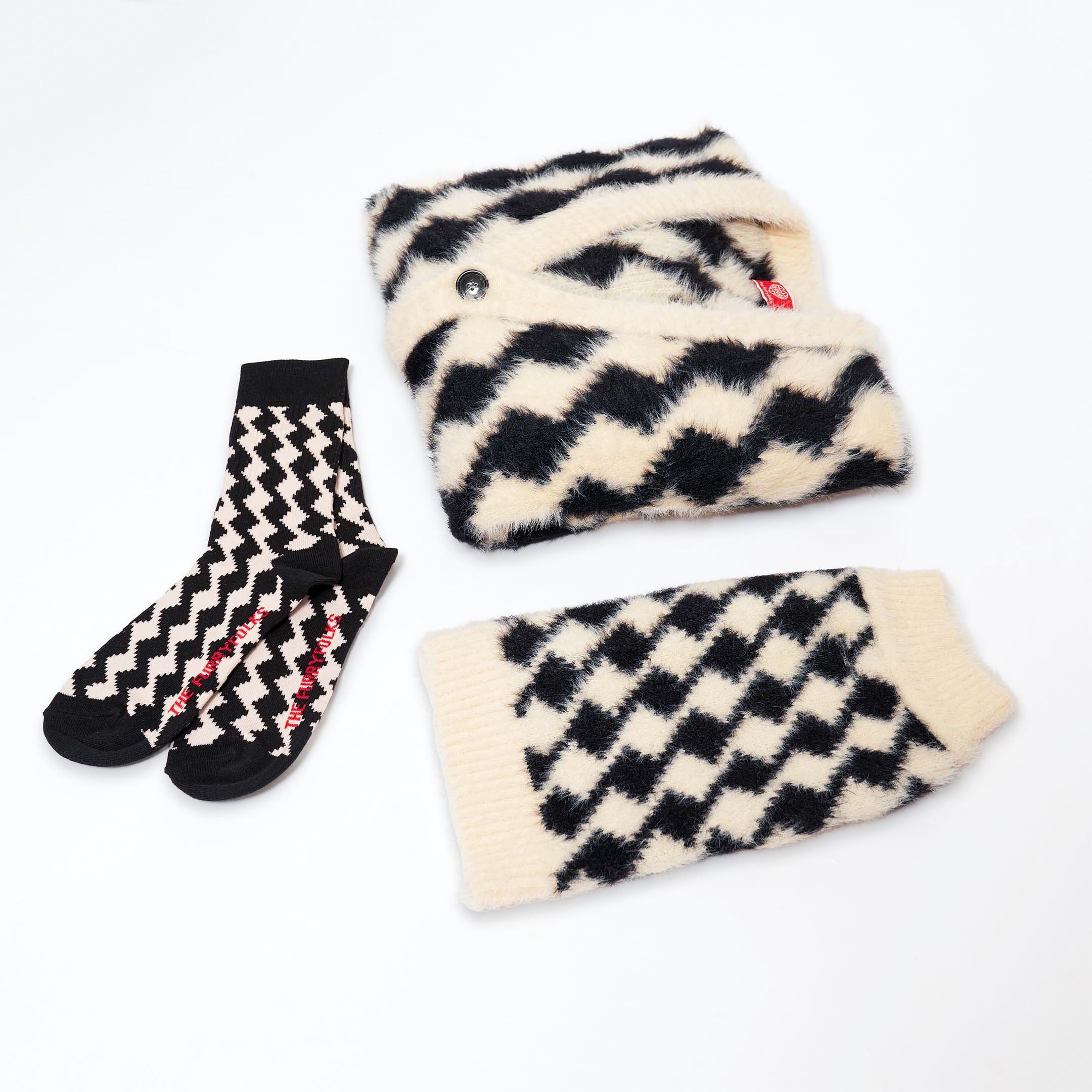 This image features a black and white zigzag patterned matching set. It includes a pair of socks with a bold zigzag design, a cozy sweater with the same zigzag pattern for humans, and a matching sweater for pets. The socks have "THE FURRY FOLKS" written in red on the foot. The overall design is stylish and modern, combining a monochromatic color scheme with a striking pattern, perfect for coordinated outfits for humans and their pets.