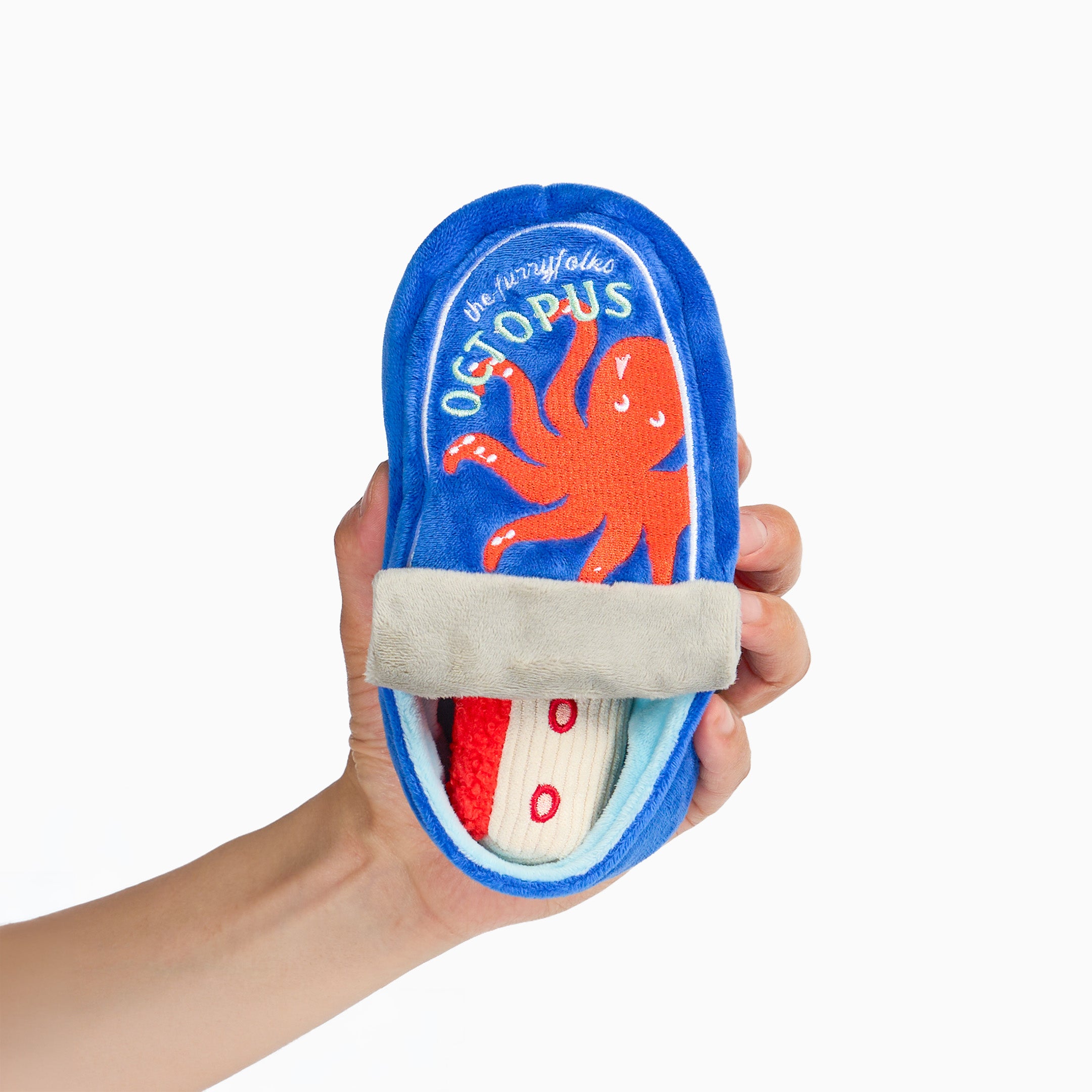 A hand holding a blue plush baby bootie with an orange octopus design and the word 'Octopus' on the sole, against a plain white background.