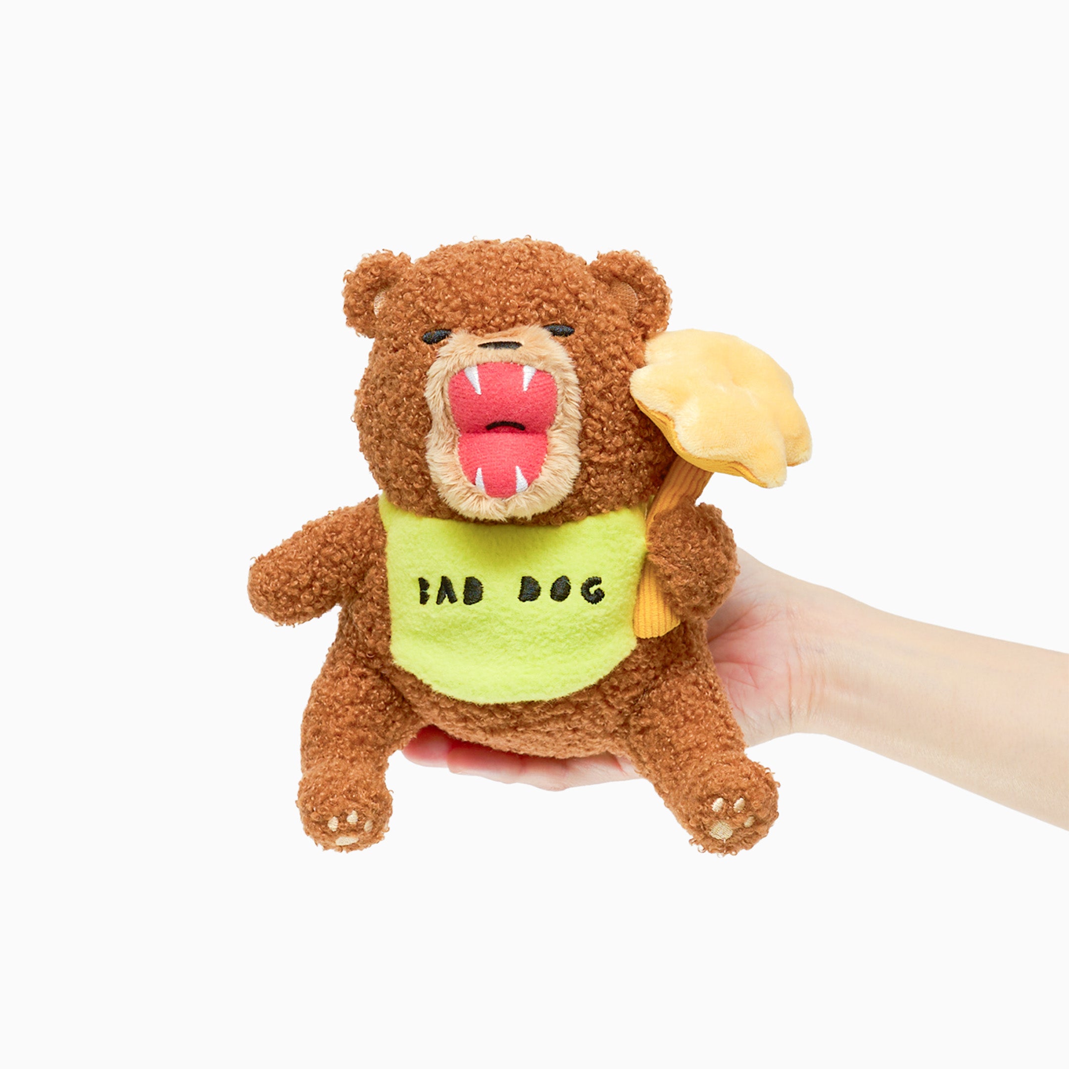 Plush toy bear with a green shirt labeled 'Bad Dog' held by a hand on a white background