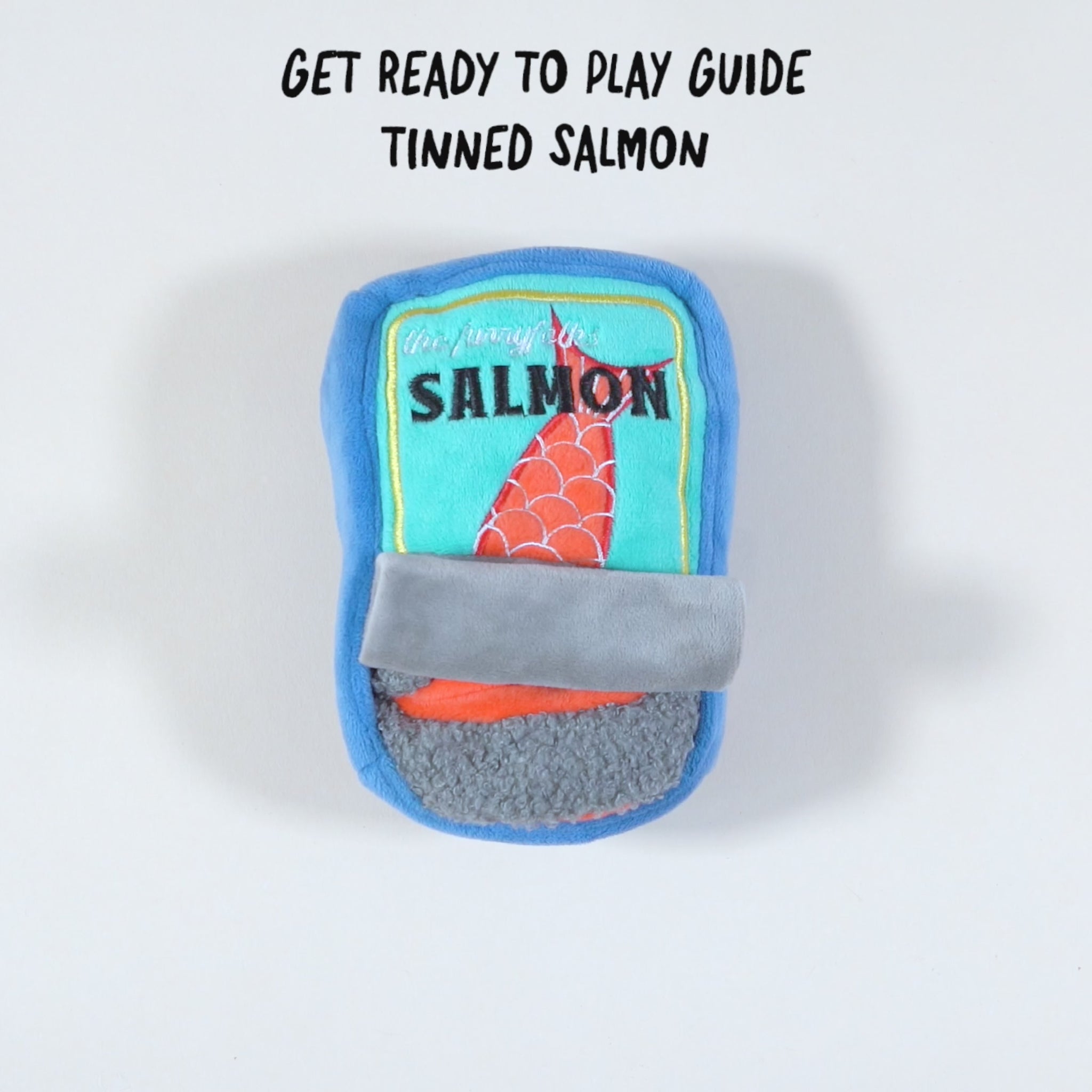 The video likely features a plush dog toy shaped like a can of salmon. The toy is blue with a light blue label that includes an illustration of a red fish tail and the word “SALMON.” There might be scenes showing the toy being used for dog nosework activities, possibly with a dog interacting with or playing with the toy. The video may highlight the design details and functionality of the toy, including any hidden compartments or features that make it engaging for pets.