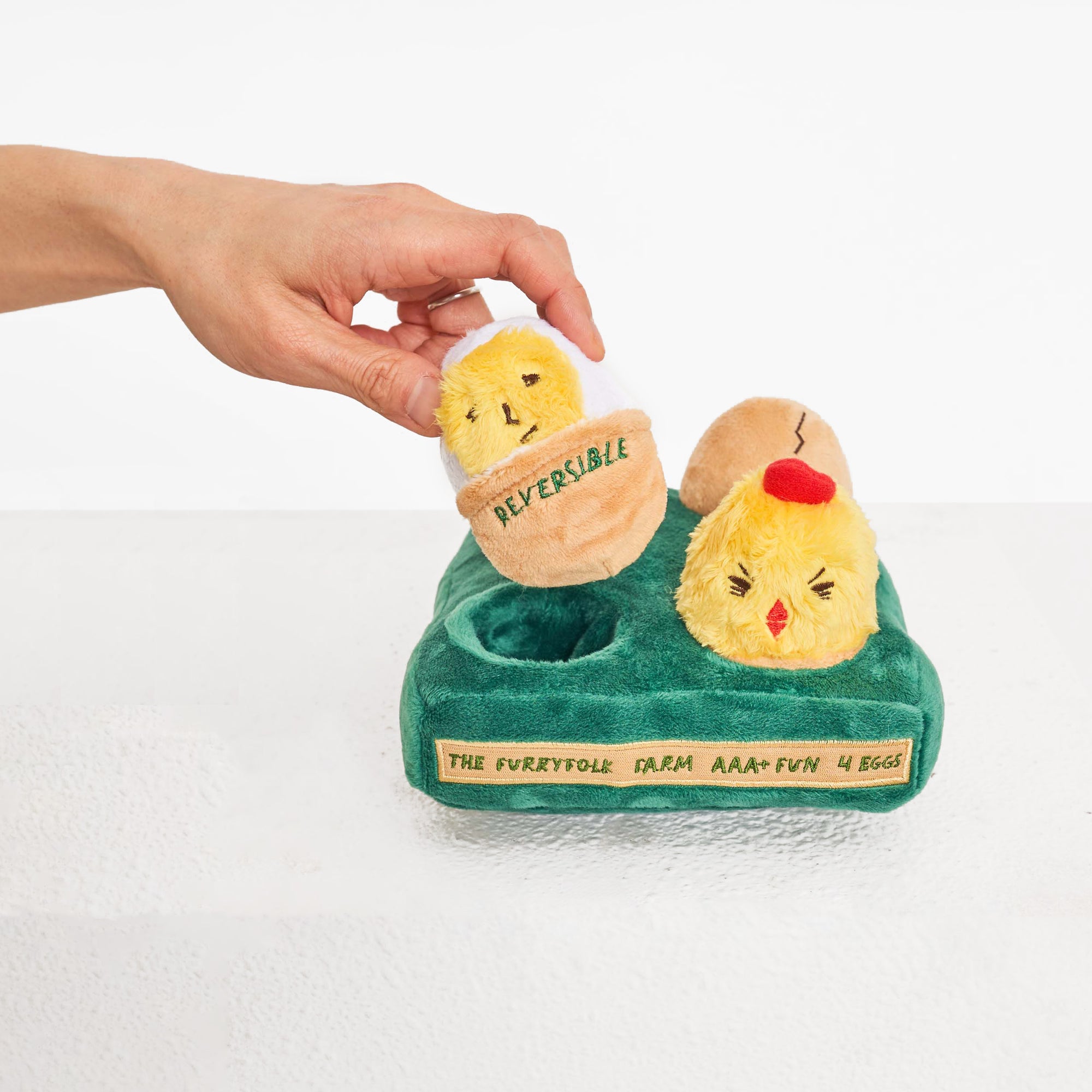 Hand picking a reversible chick plush from a farm-themed dog puzzle toy.