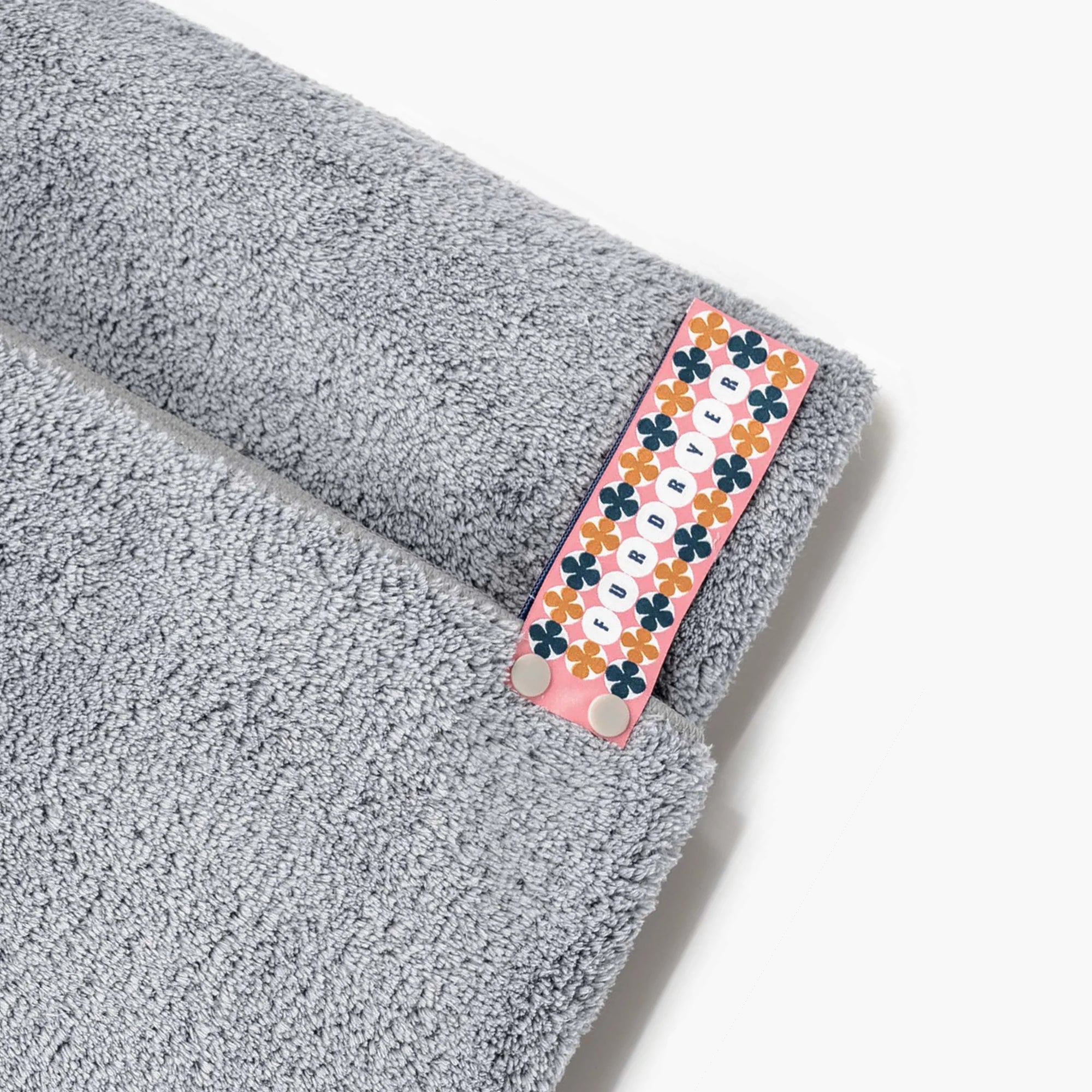 Close-up of a soft, fluffy grey dog towel with a charming floral and geometric patterned tag. The tag adds a touch of whimsy and design detail, making this absorbent towel not just a pet care necessity but also a delightful accessory for your furry friend's bath time.