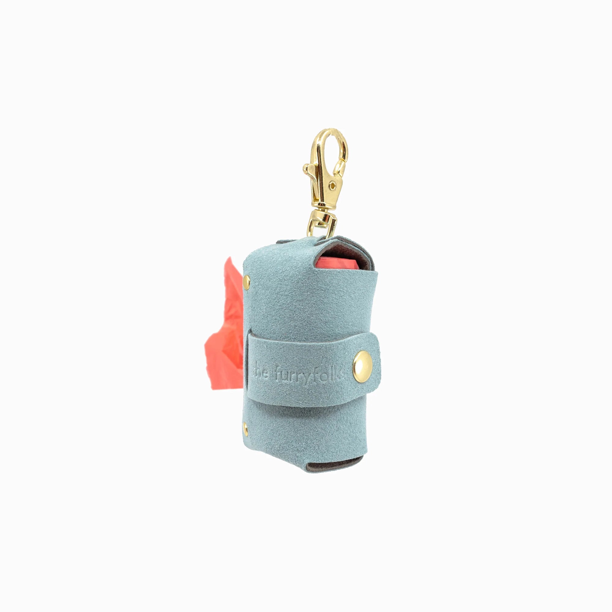 The image features a sky blue dog poop bag holder with a roll of red bags slightly visible, equipped with a gold clip for attachment. It's marked with "the furryfolks" branding, designed for convenience during dog walks.