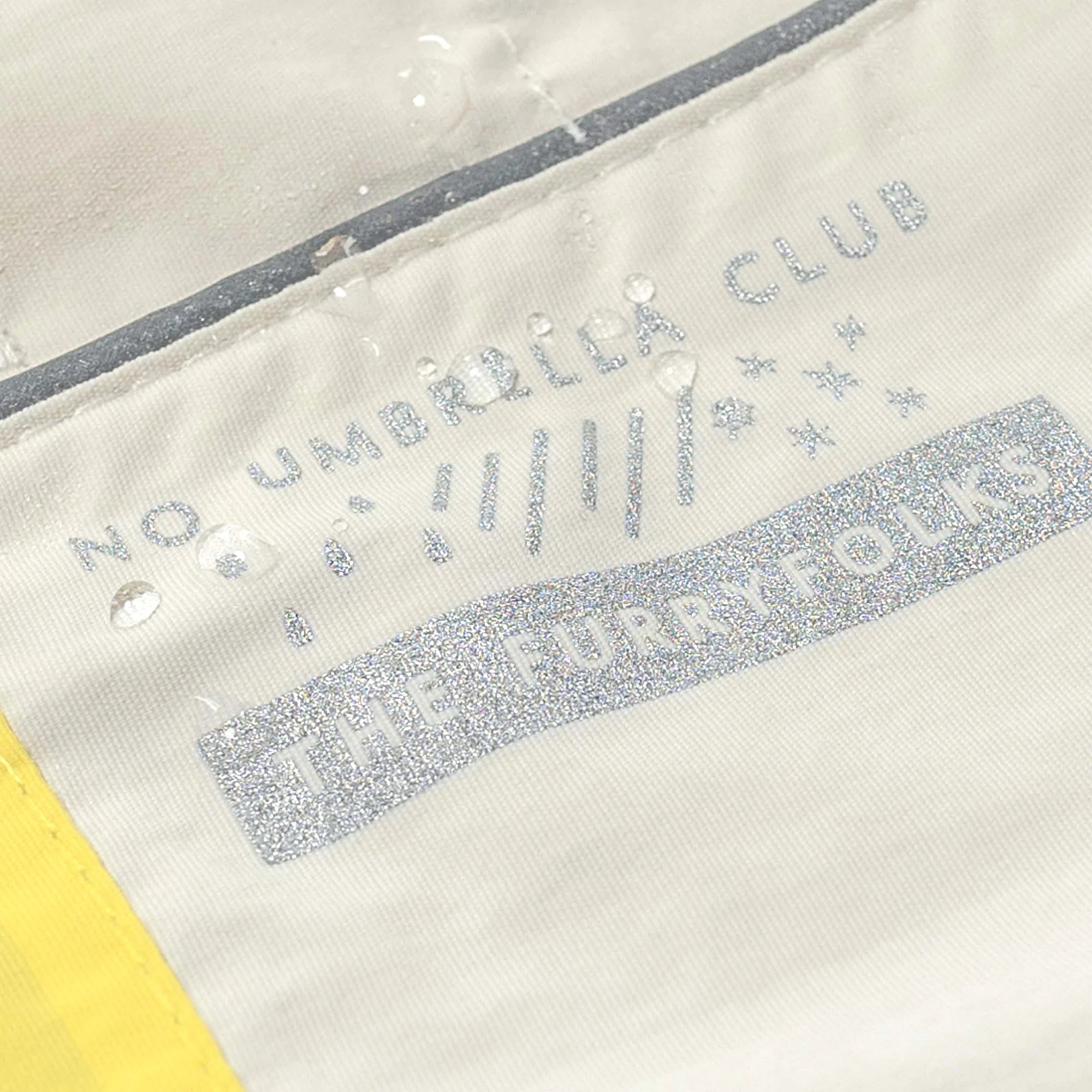 Water-resistant dog coat detail with 'The Furryfolks' logo and 'No Umbrella Club' print.